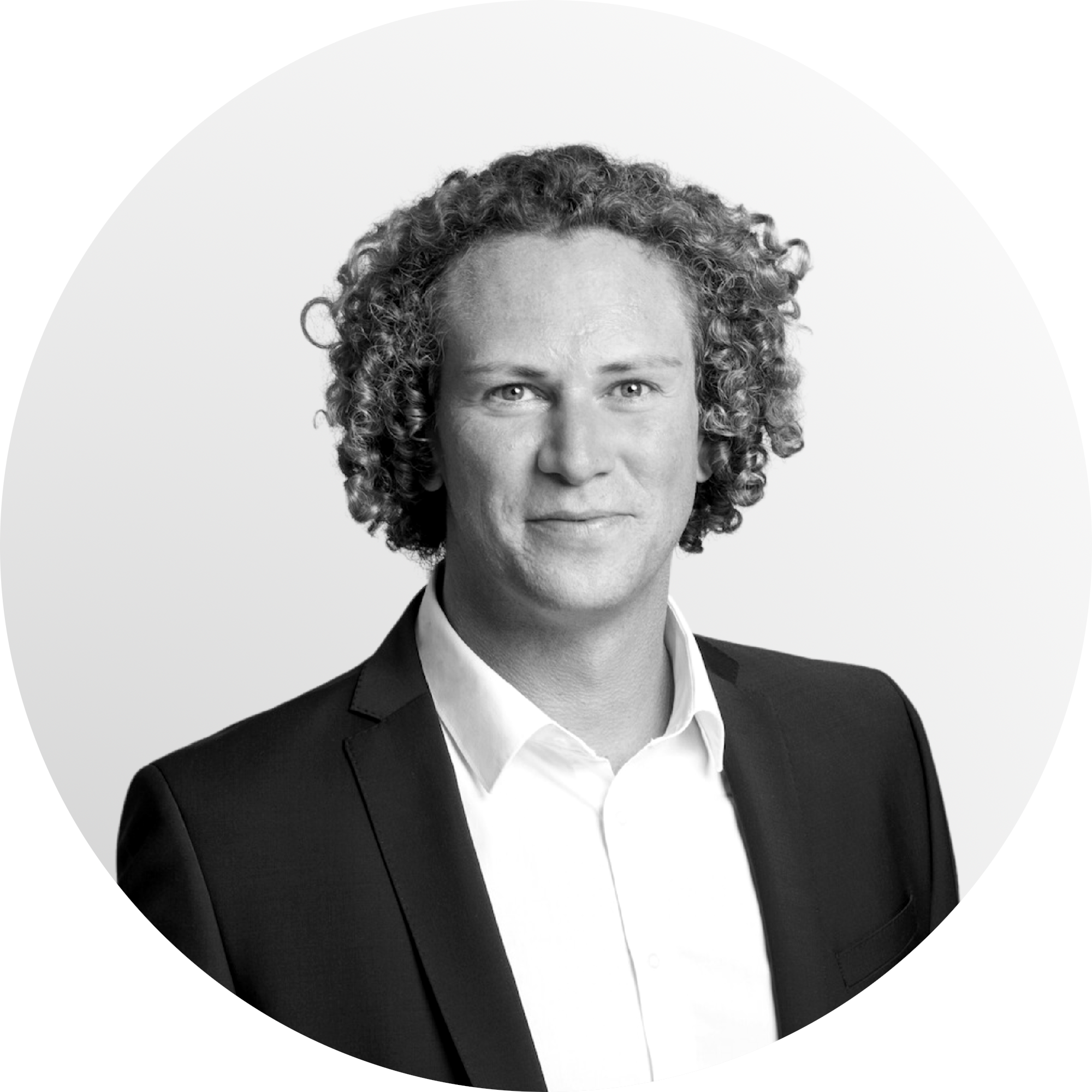 Black and white portrait of a smiling man with curly hair, wearing a suit jacket and white shirt, against a plain background.