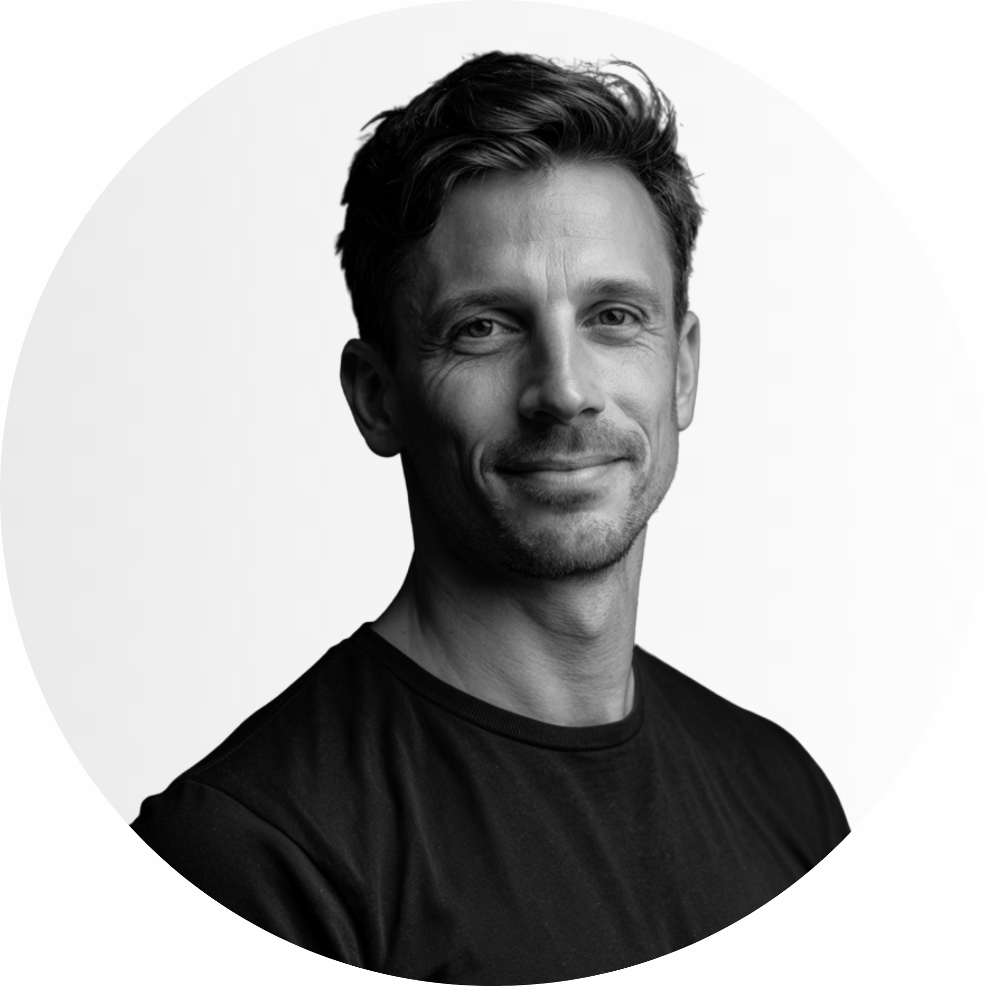 Ein Mann mit kurzen Haaren und einem leichten Lächeln, der ein einfaches dunkles T-Shirt trägt, posiert vor einem hellen, einfachen Hintergrund.