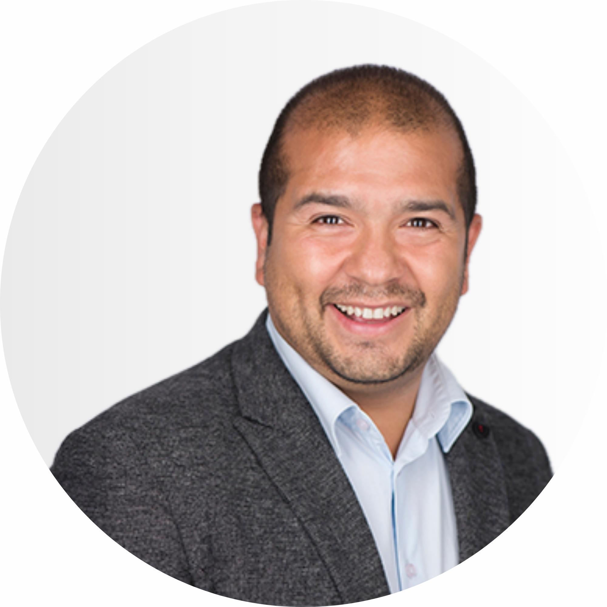 Ein Mann mit kurzen Haaren und Bart lächelt, er trägt einen grauen Blazer und ein helles Hemd, vor einem schlichten weißen Hintergrund.