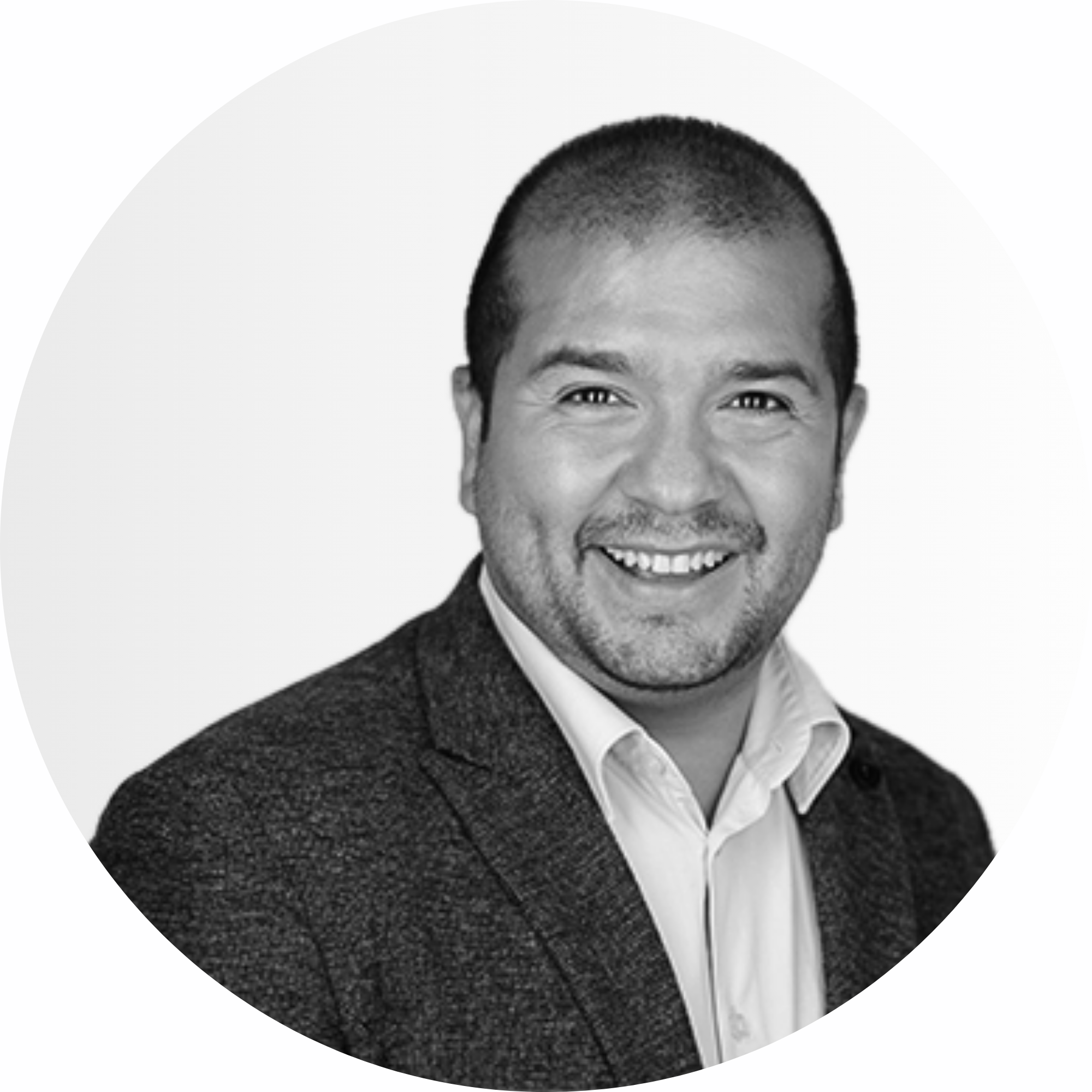 Ein Mann in Anzugjacke und Kragenhemd lächelt in die Kamera vor einem schlichten, hellen Hintergrund.